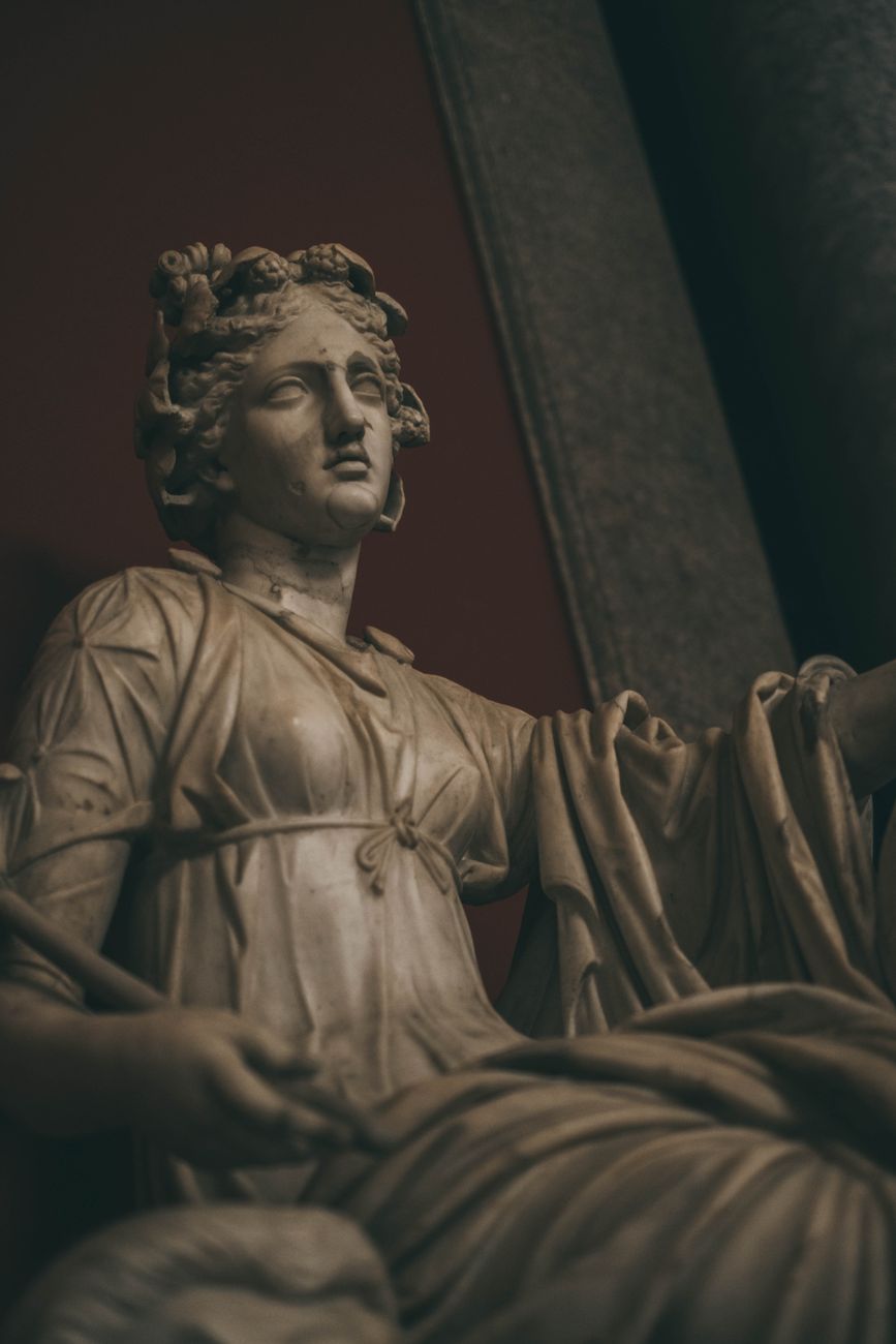 Close-up of a marble statue depicting a seated figure, possibly a goddess, with detailed facial features and intricate drapery.